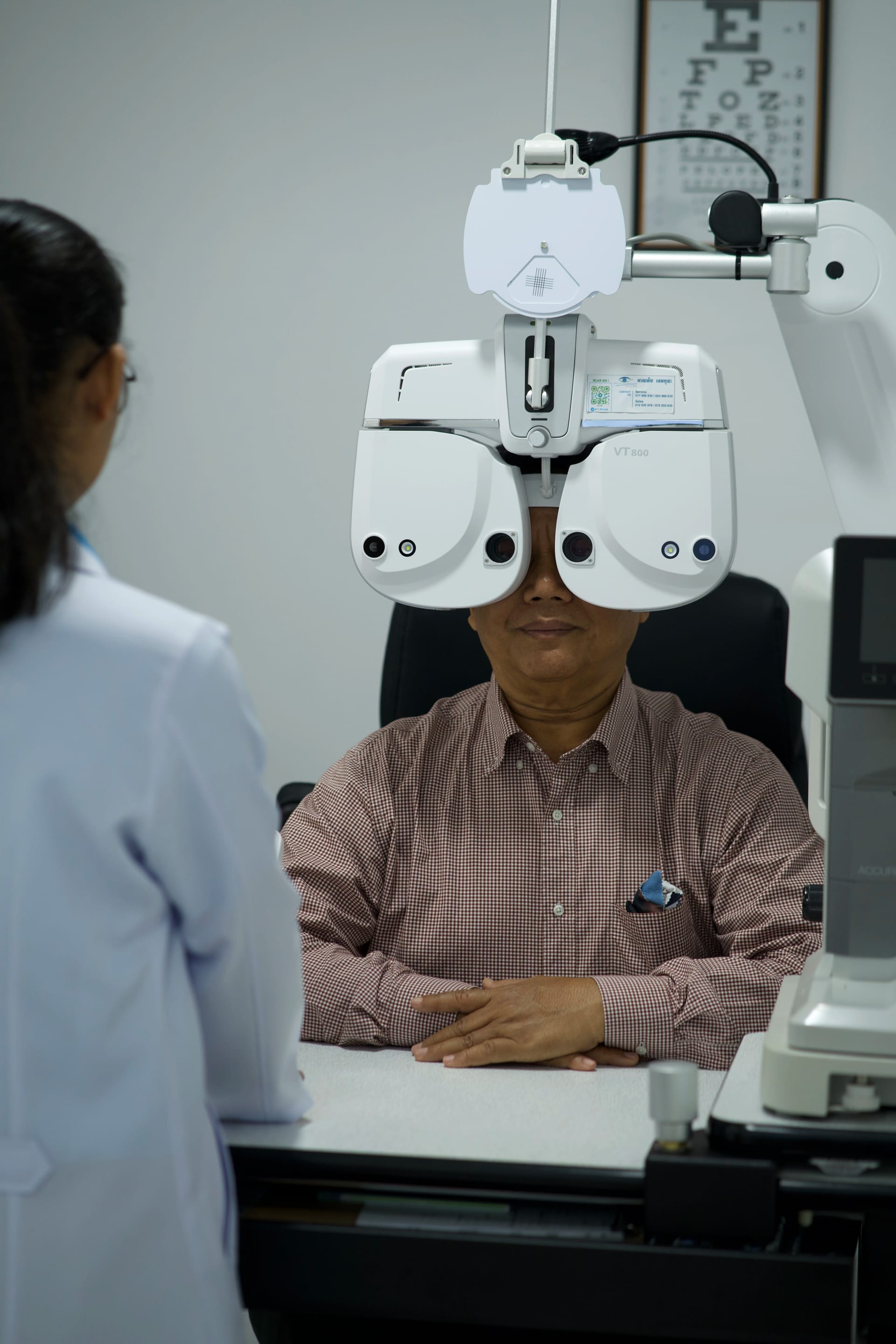 Patient receiving precision digital phoropter eye examination for custom prescription eyeglasses at M-Optic Cambodia